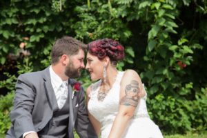 Bride and groom sitting in front of a lush green background. Photo by Melanie Taylor Photography.