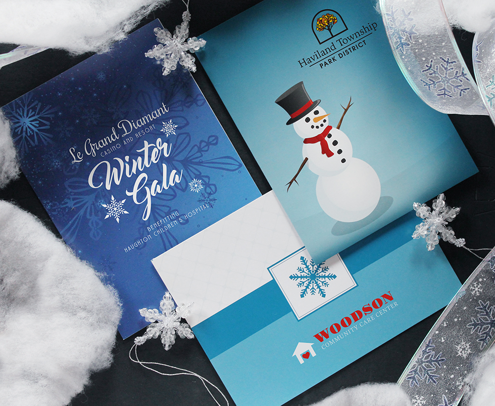 Three blue winter-themed photo folders with event branding and company logos printed on the front covers