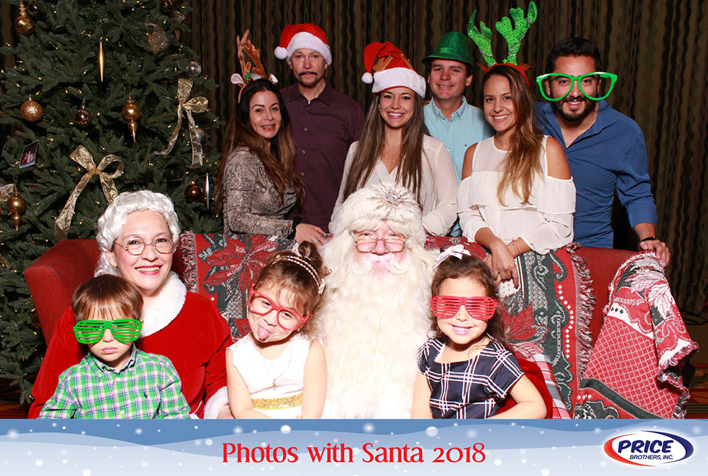 A large group of people wear silly glasses and other props while having their picture taken with Santa and Mrs. Claus.