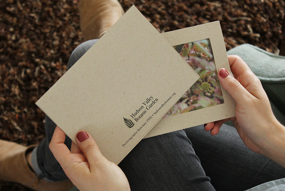Woman holding a recycled kraft paper photo insert card. Back of card has a black logo imprint for a botanic garden.
