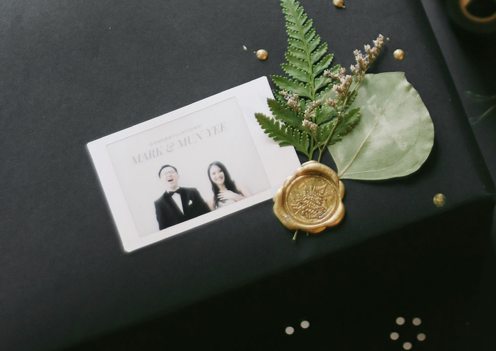 Instax Mini print of a bride and groom lays on a black table with a gold seal and leaf decorations