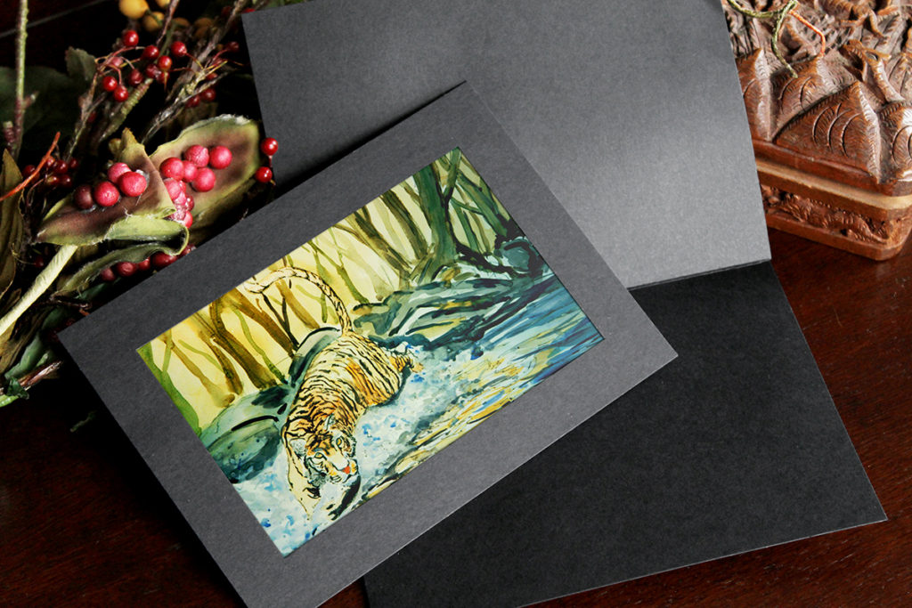 Black photo insert card holds a watercolor print of a tiger splashing through a river in the forest.
