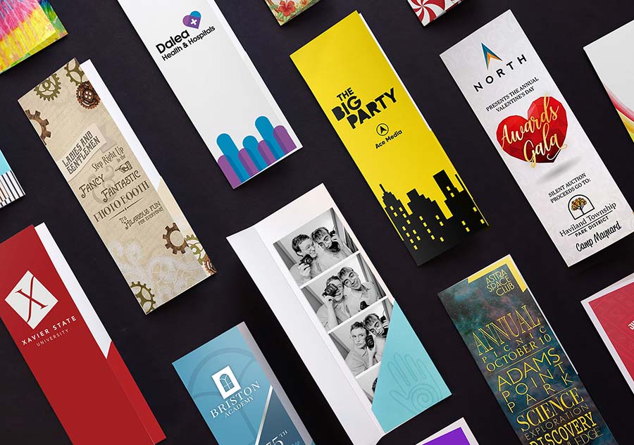 A collection of 2 by 6 photo booth folders lay on a table, each with event branding and logos