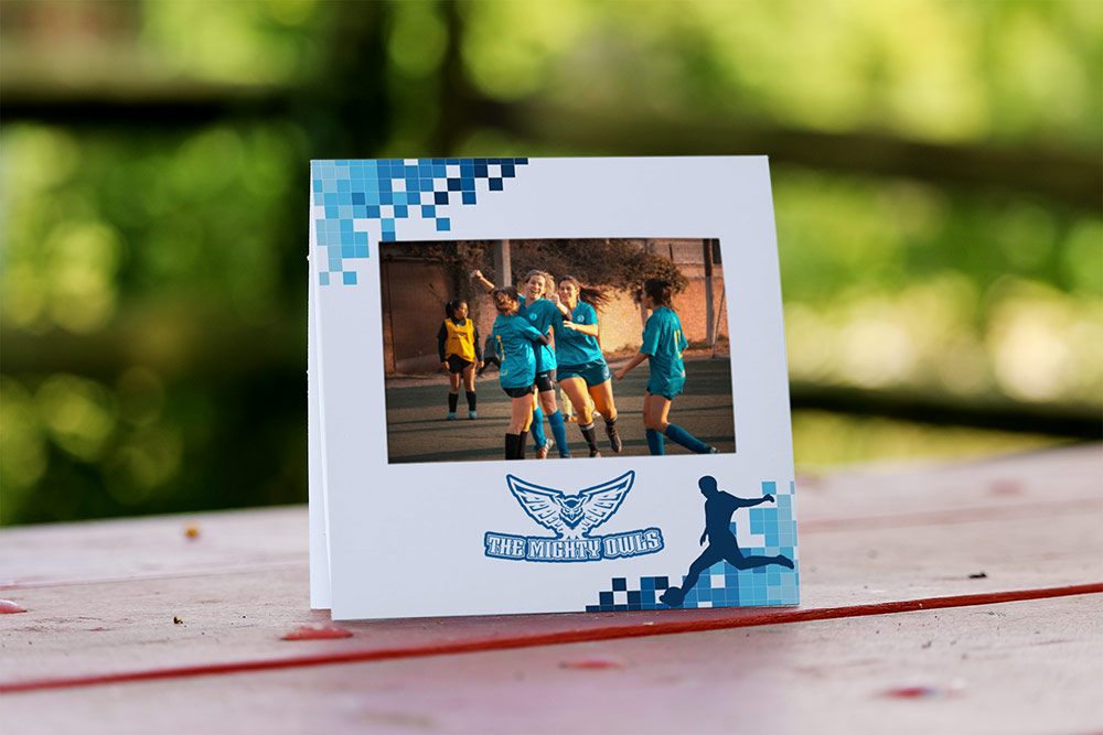Instax paper frame sits outside on a red picnic table. Frame has a team mascot and soccer design.
