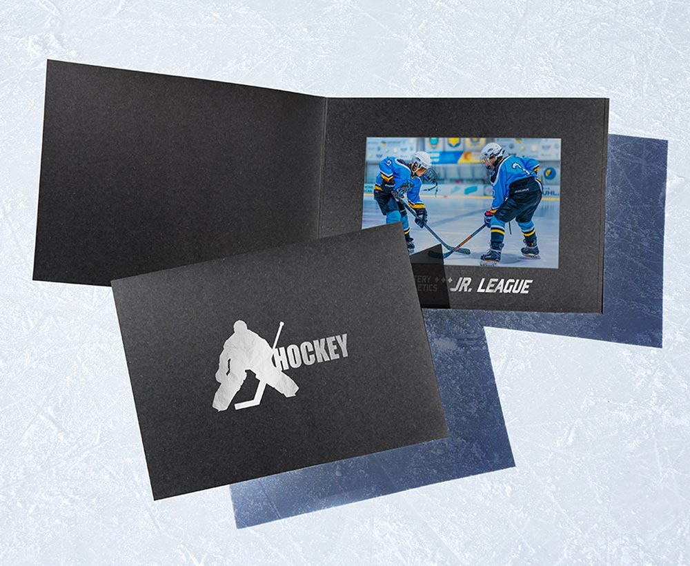 Black horizontal photo folder with silver foil hockey player design on the front cover and team name stamped on the inside window frame border.
