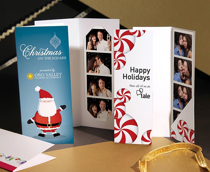 Two Chirstmas-themed photo booth picture strip folders, each with event branding printed on the front covers.