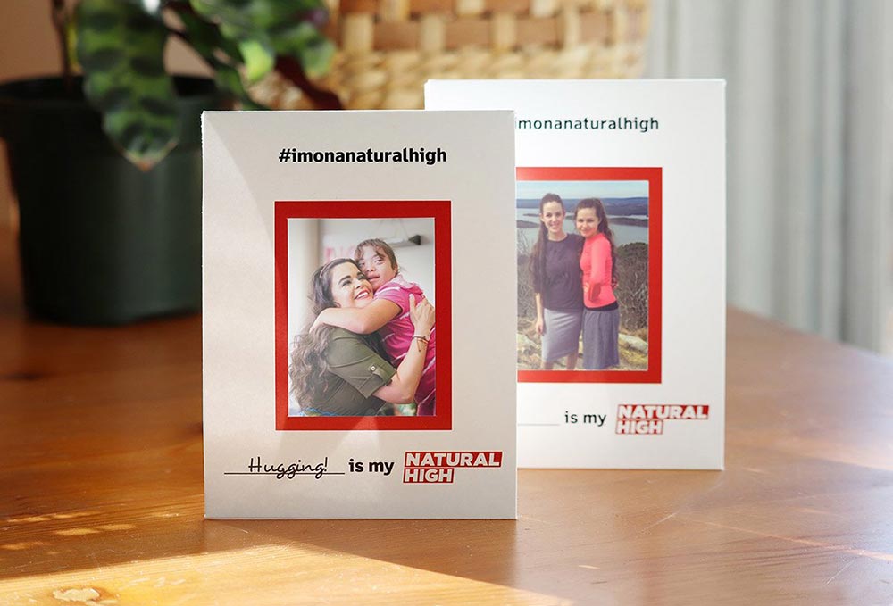 Two Instax Mini paper frames sit on a kitchen table. Each frame has a hashtag that reads 'I'm on a natural high' and an area below the photo for people to write what their natural high is.
