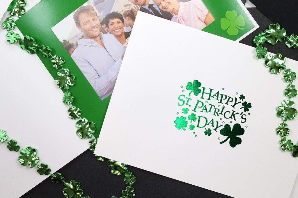 Two St. Patrick's Day photo folders, one with a metallic green foil imprint on the front cover, the other printed green inside with a four-leaf clover. Green shamrock beads surround the folders.