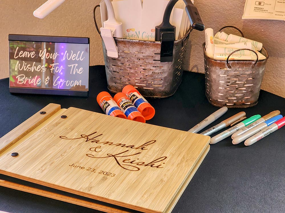 A scapbook, Sharpie markers, glue sticks, and two metal buckets with lip balm and photo folders with on a table by a photo booth.