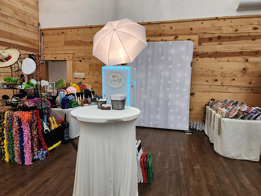 Photo booth set up for CaptureME, with a white backdrop and full prop tables on each side.