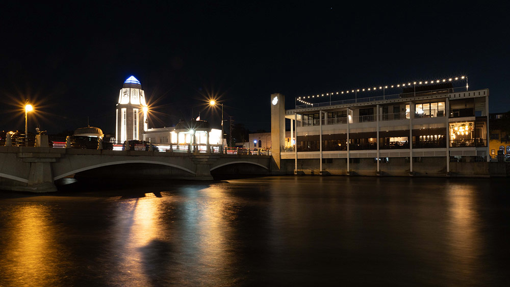 A river at night with light reflecting in the river. The water looks smooth because the shutter was open for 25 seconds.