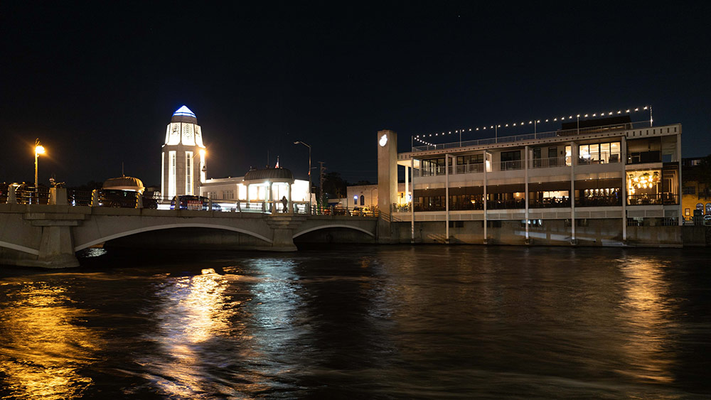 A river at night, surrounded by brightly-lit buildings and a bridge.