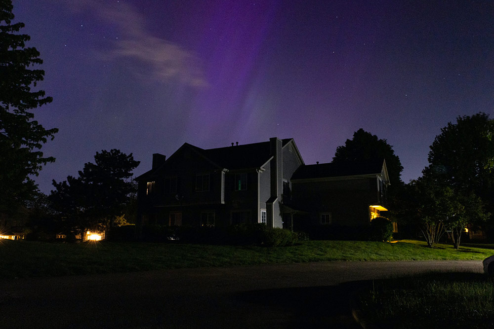 The northern lights appear over a house, in subtle shades of purple.