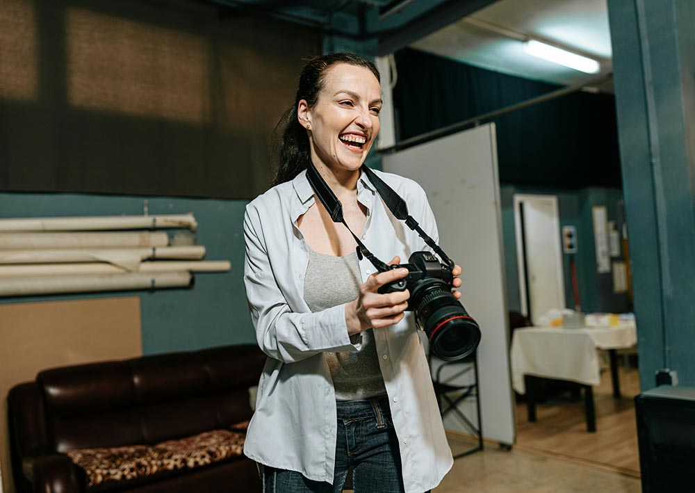 A woman holds her camera while laughing.