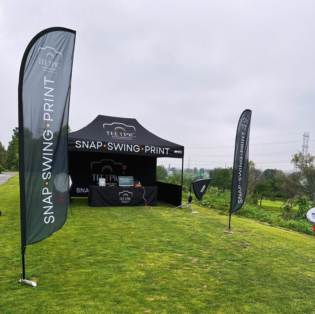 Tee Pic Photography's setup at a golf event, includes a tent, banners, and lighting with a scenic background.